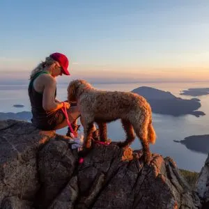 Goldendoodle and women on peak above lake